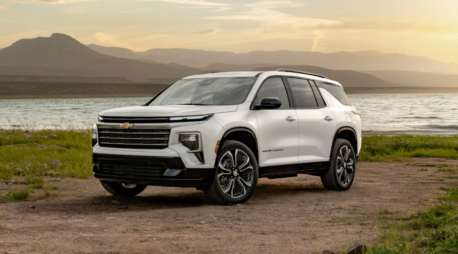Exterior front three-quarter view of the luxury 2027 Chevrolet Traverse High Country trim in white with chrome grille accents and polished wheels parked near a lake, available at Elkins Chevrolet in Marlton, NJ