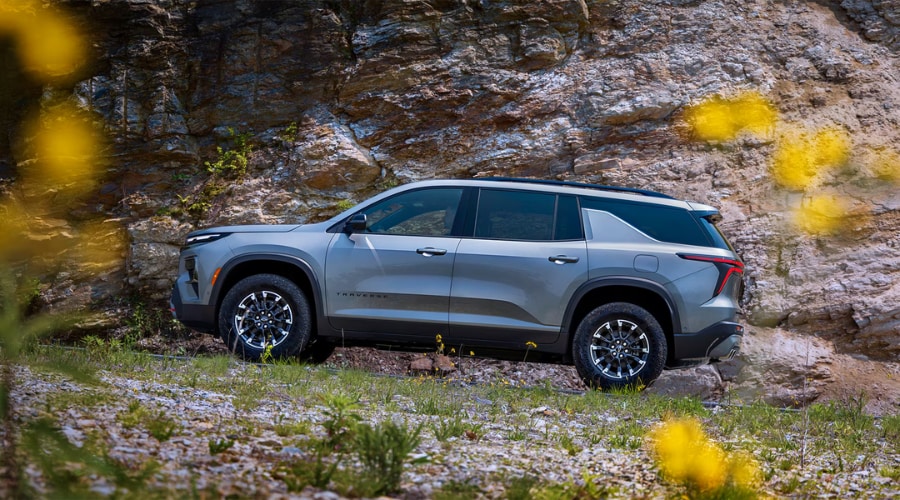 Silver metallic CarBravo certified pre-owned 3-row Chevy Traverse Z71 SUV parked in profile against a rugged rocky cliff face, highlighting family utility and off-road capability for South Jersey drivers in Marlton and Mt. Laurel, NJ.