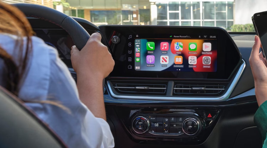 Driver perspective inside a 2026 Chevy Trax showing the 11-inch touchscreen running wireless Apple CarPlay with active map and music app icons, demonstrating hands-free smartphone pairing available at Elkins Chevrolet in Marlton, NJ.
