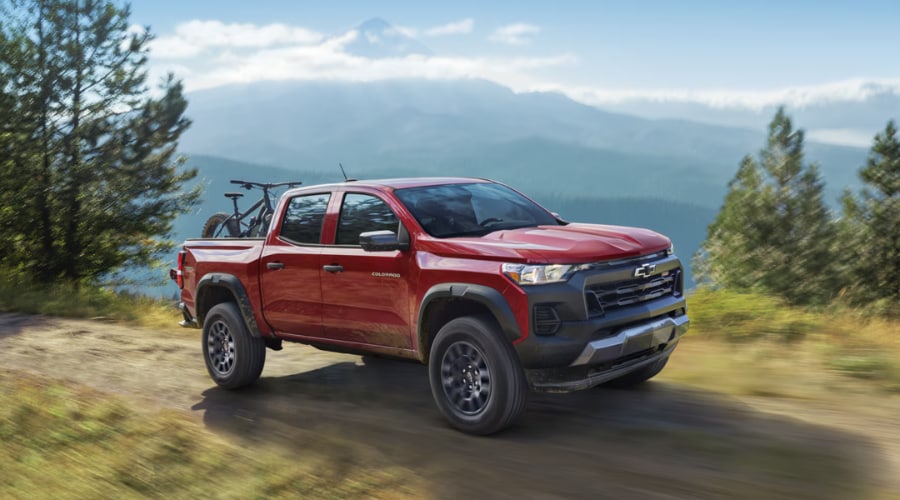 Side profile of a red 2026 Chevy Colorado hauling a mountain bike on a forest trail, demonstrating the versatile carrying capacity evaluated in our 2026 Chevy Colorado Highway Review near Marlton, NJ.