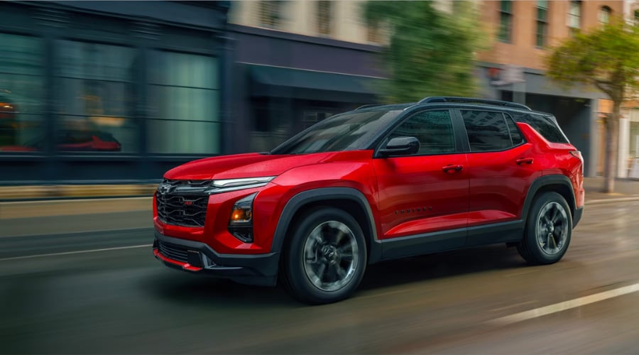 A red 2026 Chevy Equinox RS with a black roof driving past Cherry Hill buildings, showcasing the bold front fascia and redesigned athletic exterior styling of this compact SUV