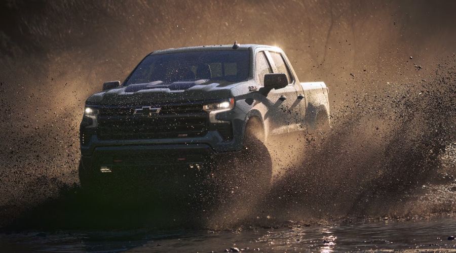 CarBravo certified pre-owned dark gray Chevy Silverado 1500 Z71 truck splashing through off-road mud and water at sunset, showcasing durable pre-owned performance for South Jersey drivers in Marlton and Deptford, NJ.