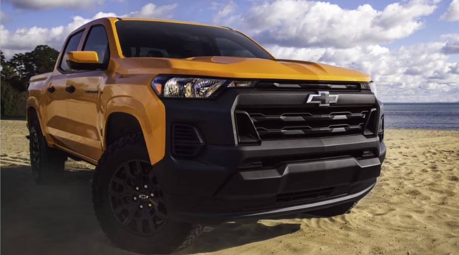 A bright yellow 2026 Chevy Colorado WT parked on a sandy beach under a cloudy sky, highlighting the rugged matte black front grille analyzed in our highway review for Marlton, NJ commuters.