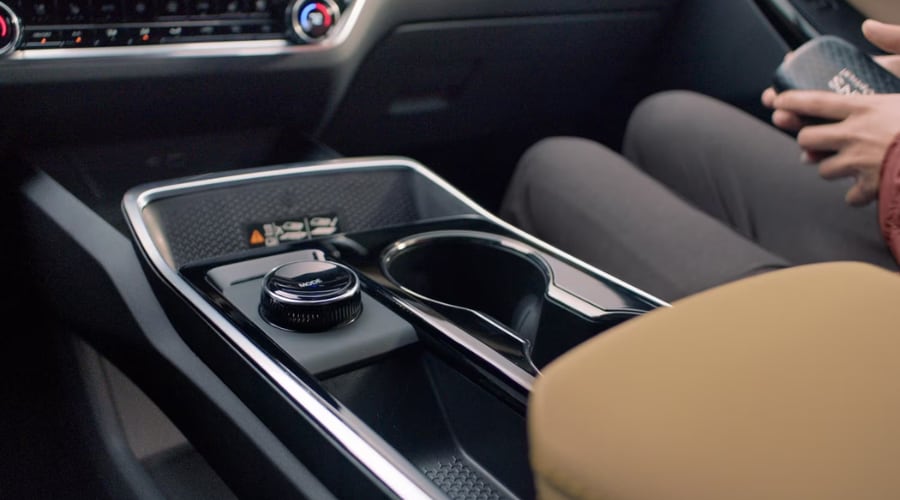 The interior center console of a 2026 Chevy Equinox ACTIV in Marlton, NJ, highlighting the tactile physical rotary drive-mode selector dial, cup holders, and premium stitched tan armrest