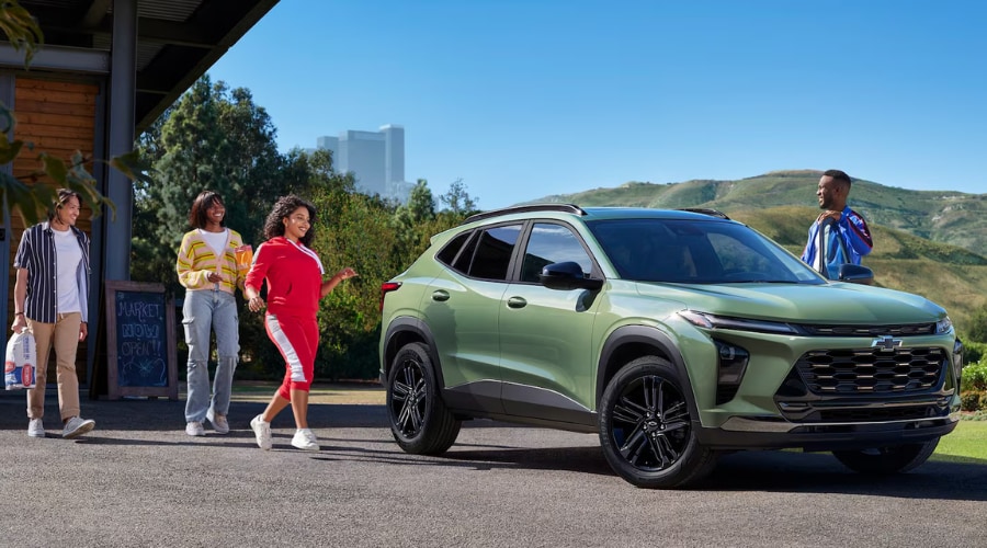 A green 2026 Chevy Trax crossover parked outside a local market with a group of friends, showcasing affordable SUV cargo space and practical utility for South Jersey commuters near Marlton, Cherry Hill, and Route 70.