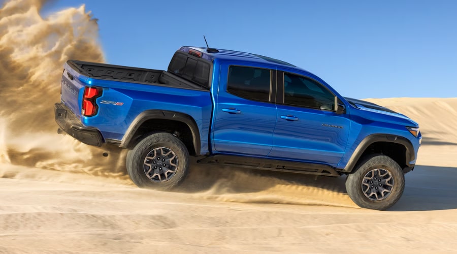 A bright blue 2026 Chevy Colorado accelerating up a sandy dune and kicking up a roost of sand, demonstrating the raw low-end TurboMax engine torque analyzed in our highway review for Marlton, NJ drivers.