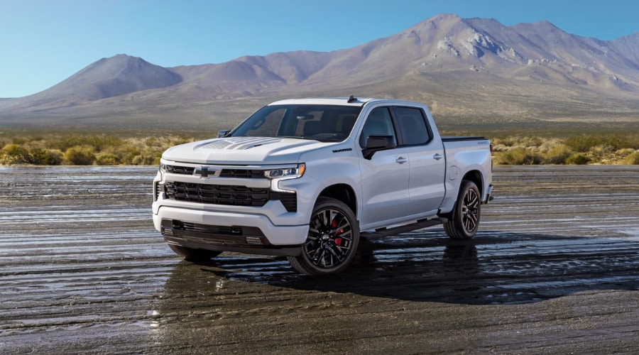Exterior front view of a white 2026 Chevy Silverado 1500 crew cab featuring a bold black front grille, LED headlights, hood graphic accents, and dark alloy wheels.