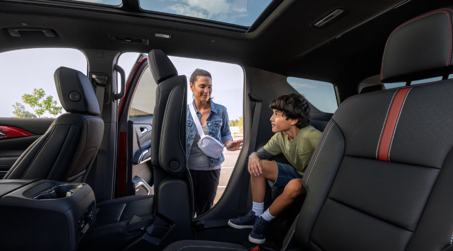 Interior view of the 2027 Chevrolet Traverse showing a mother helping her child access the third-row seating using the Smart Slide second-row seat feature, available at Elkins Chevrolet in Marlton, New Jersey.