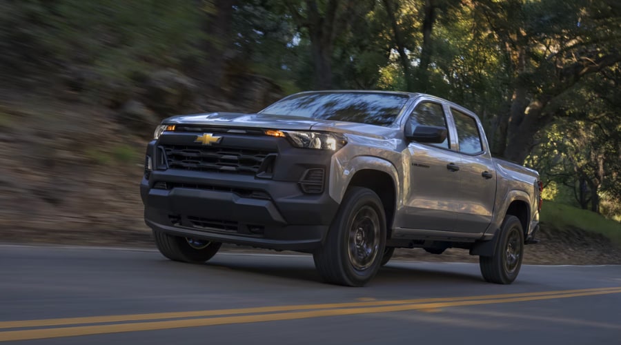 A gray 2026 Chevy Colorado WT driving along a winding, tree-lined asphalt road, showcasing the on-road handling and daily commute ride compliance evaluated in our Route 73 review near Marlton, NJ.