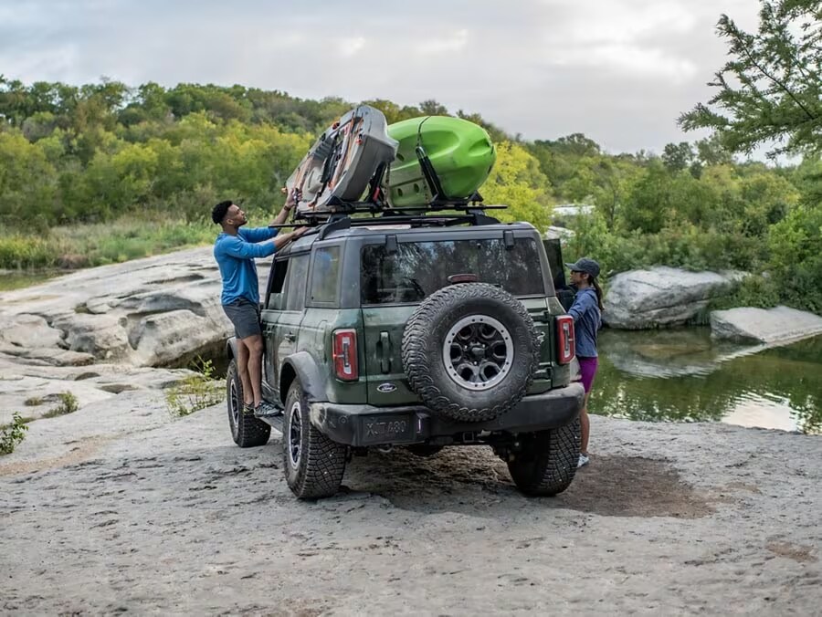 couple unloading canoes from roof rack on Ford Bronco