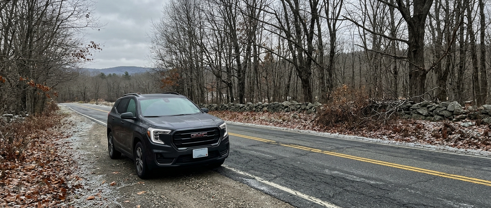 A 2026 GMC Terrain in dark metalite finish parked on a New Hampshire two-lane road lined with bare maples and the first thin frost on the pavement, overcast October sky, Monadnock.png