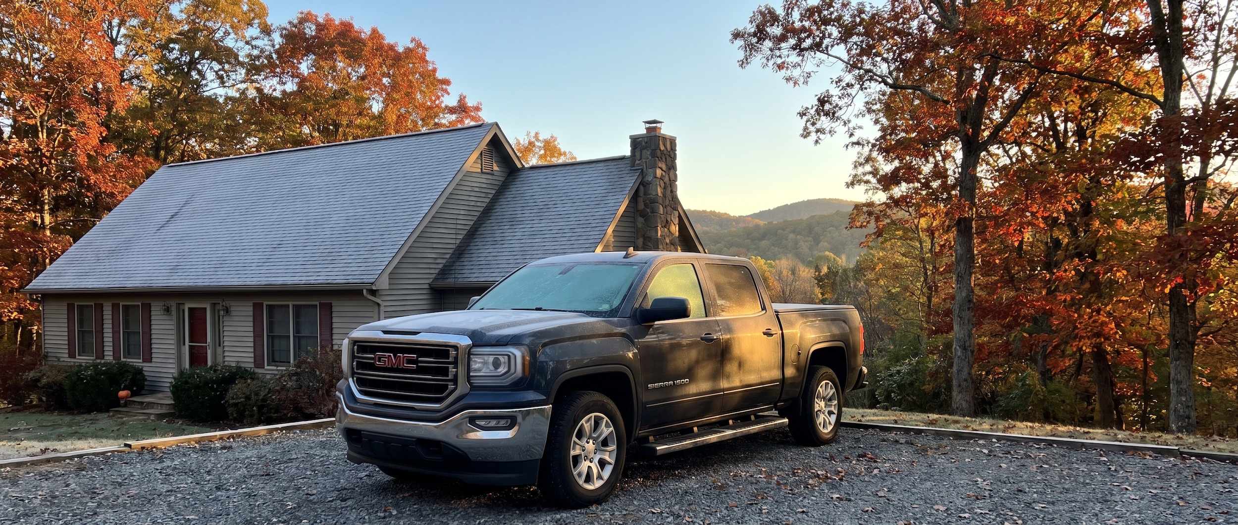 2026 GMC Yukon headlights on during fall dusk drive on a New Hampshire two-lane road with autumn foliage
