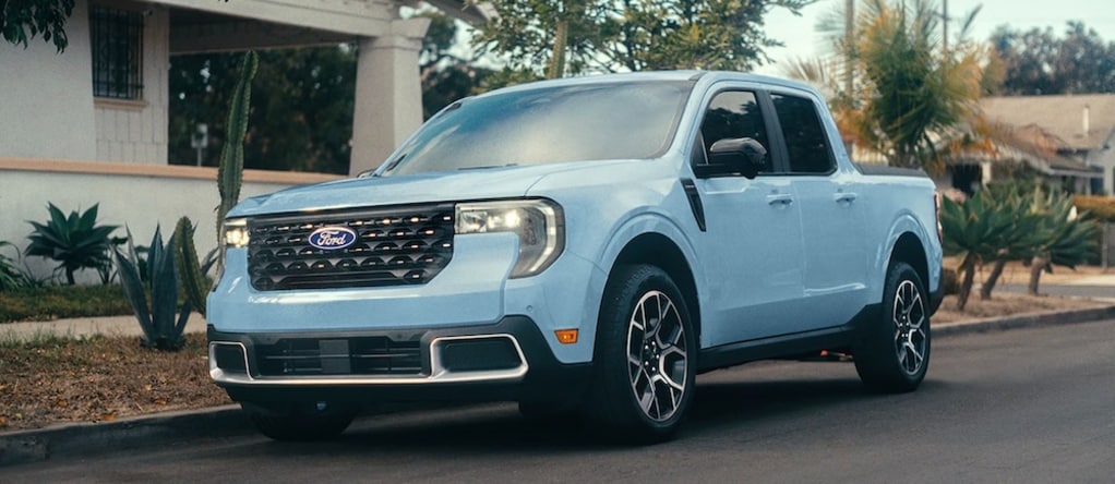 A light blue 2026 Ford Maverick parked on a residential street with cactuses and palm trees in the yard