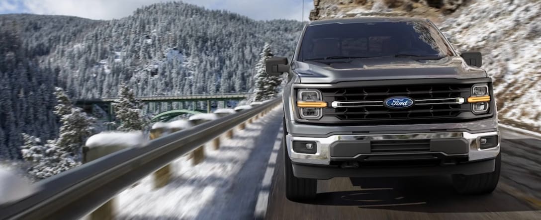 A gray 2026 Ford F-150 pickup truck driving down a snowy mountain road