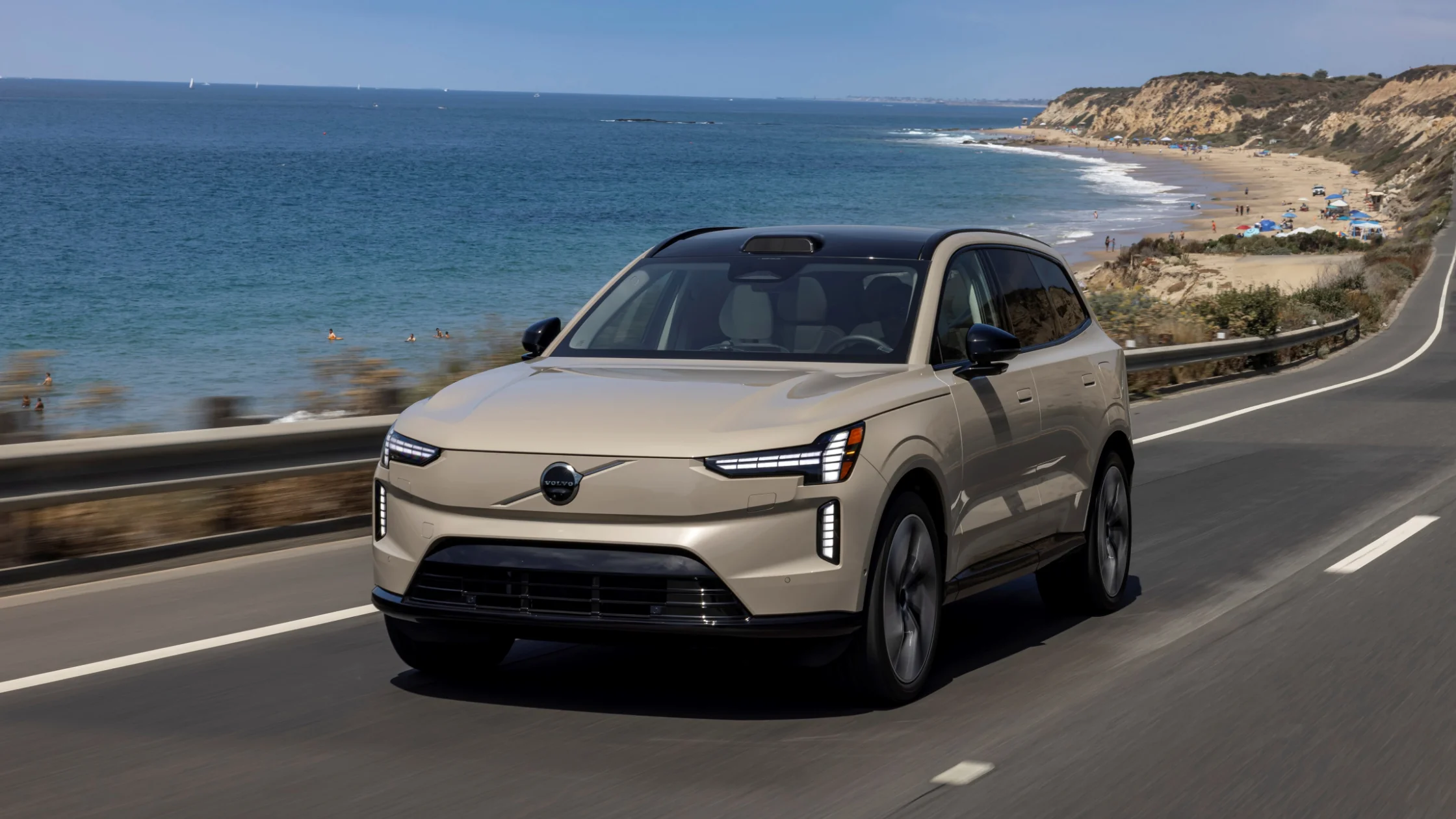 2025 Volvo EX90 electric SUV driving coastal road with ocean and cliffs in background
