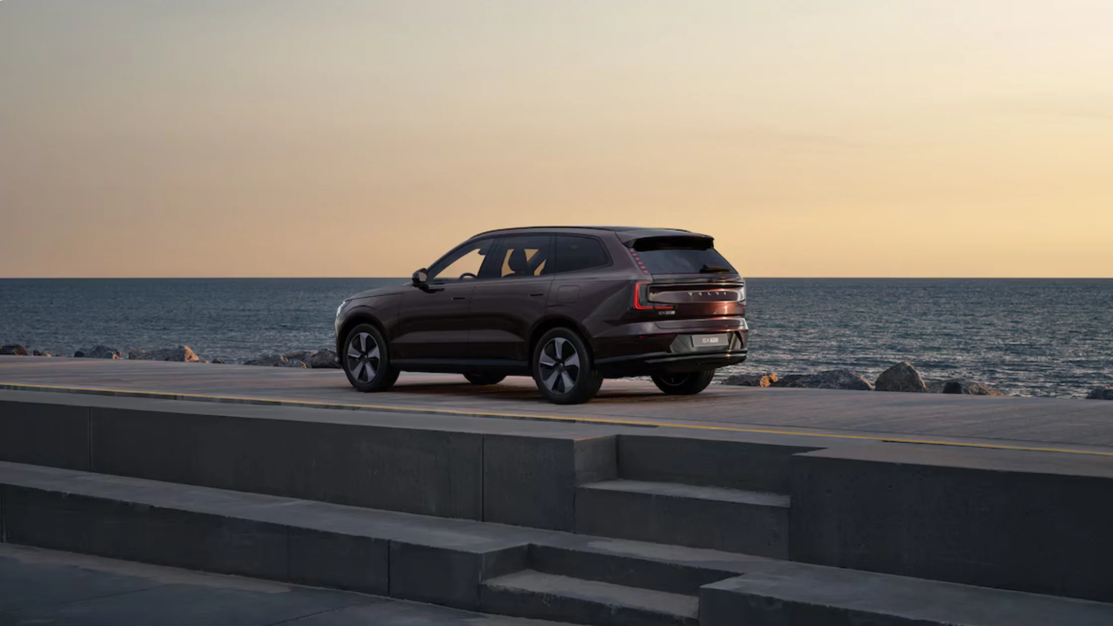 Rear view of 2025 Volvo EX90 SUV beside the ocean at dusk highlighting modern LED lighting