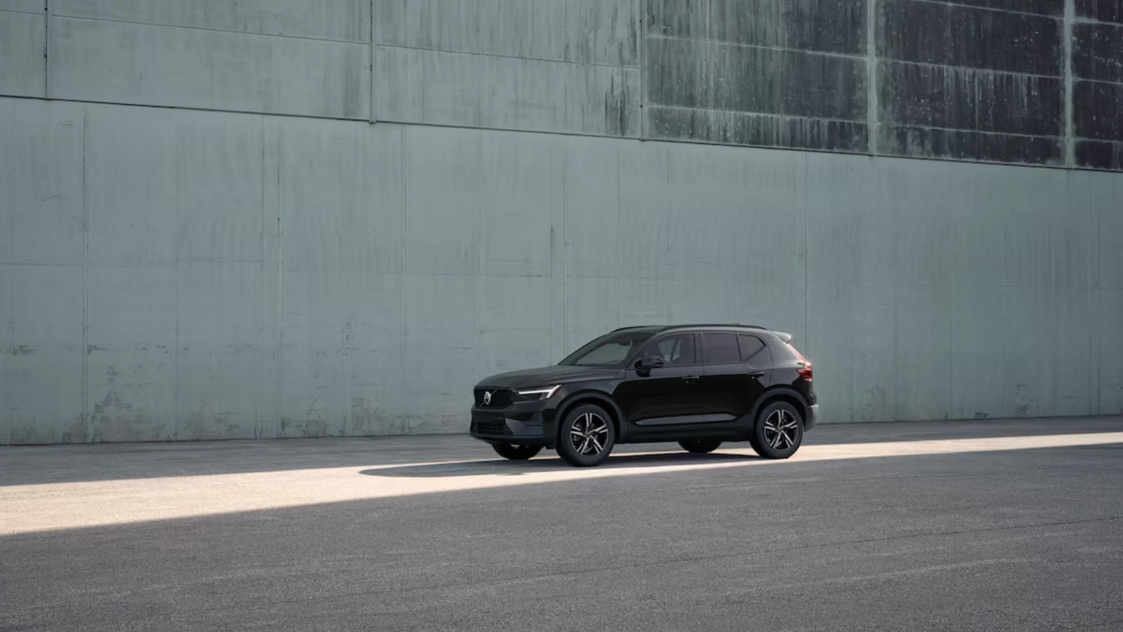 2025 Volvo XC40 in black parked beside a tall industrial wall under soft daylight