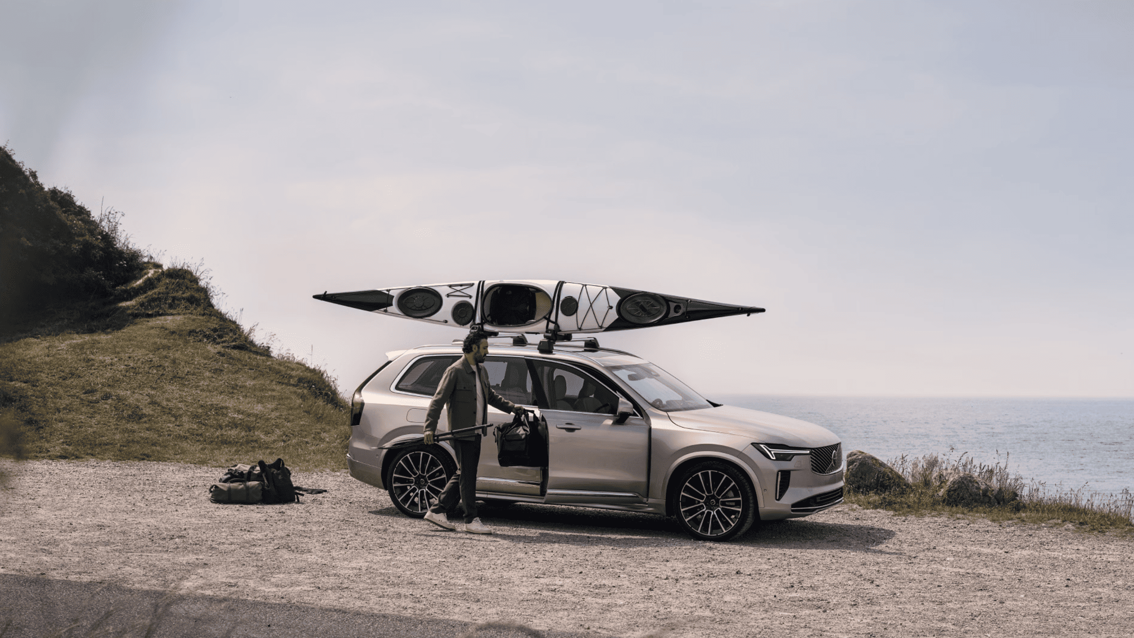 2025 Volvo XC90 luxury SUV parked by the coast with a kayak on roof, ready for outdoor adventure.