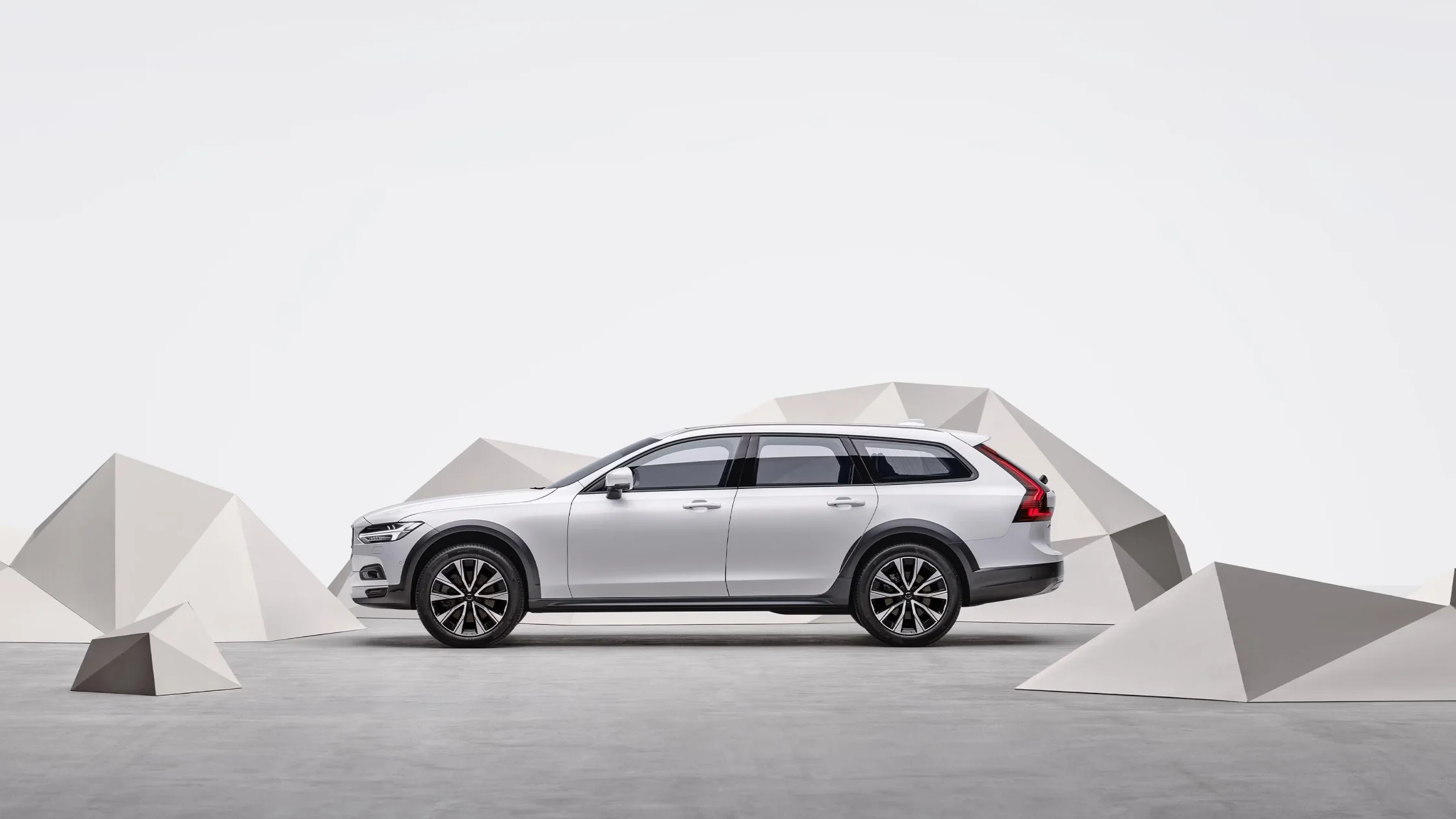 Side profile of 2025 Volvo V90 Cross Country wagon in white studio with geometric structures.