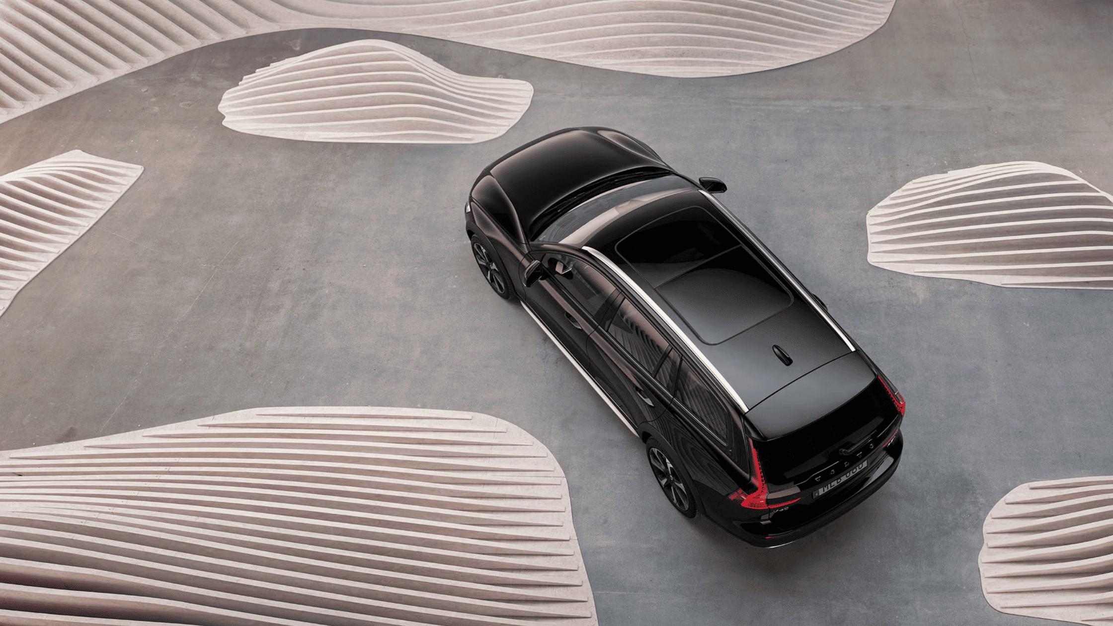 A sleek black 2025 Volvo V60 Cross Country viewed from above, surrounded by modern artistic elements