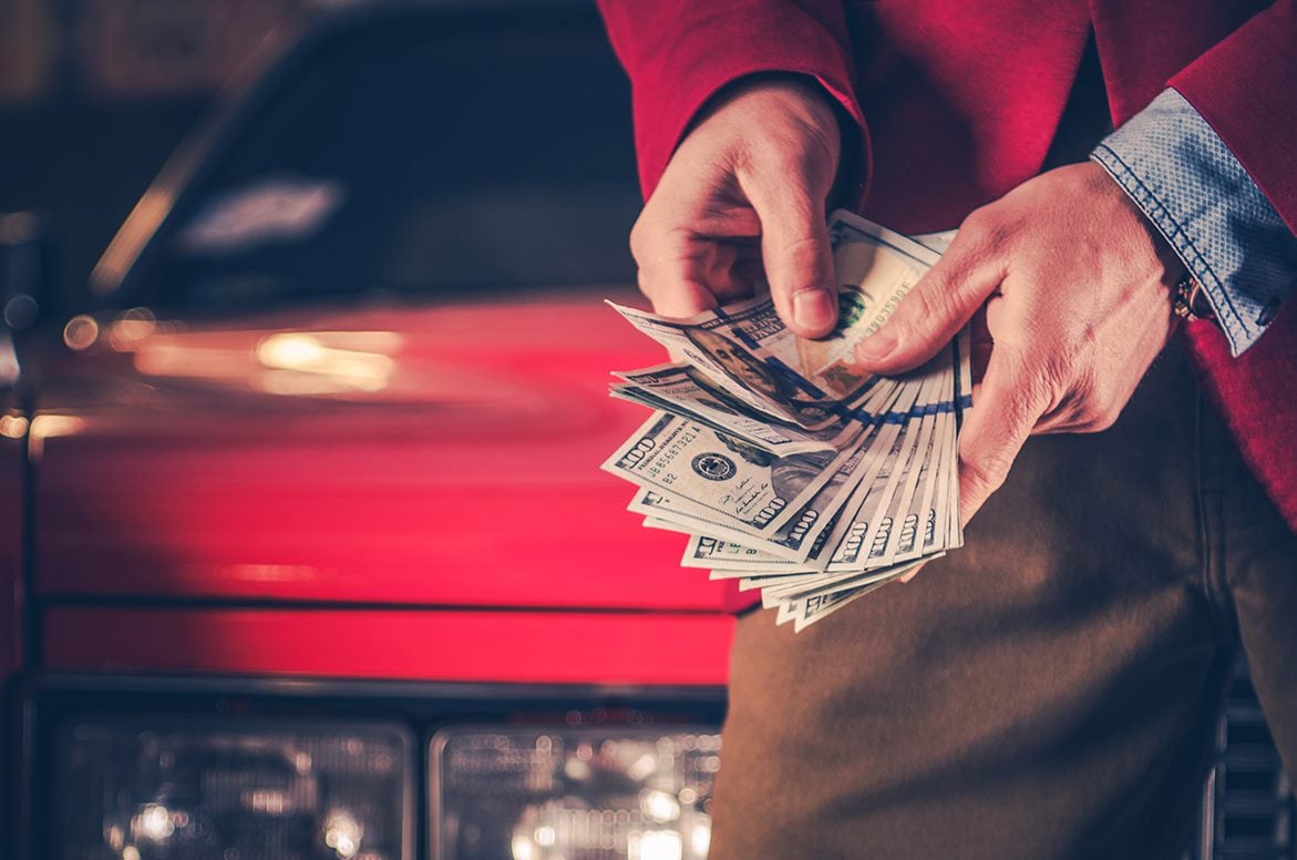 Man holding cash in front of a red car
