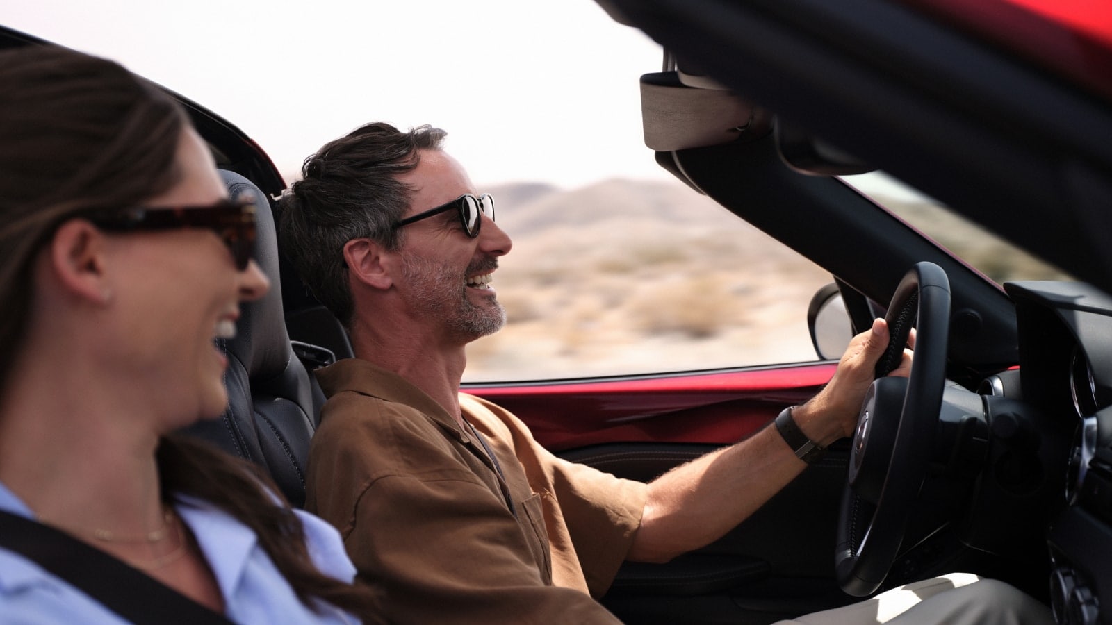 Couple driving a Mazda MX-5 Miata with the top down