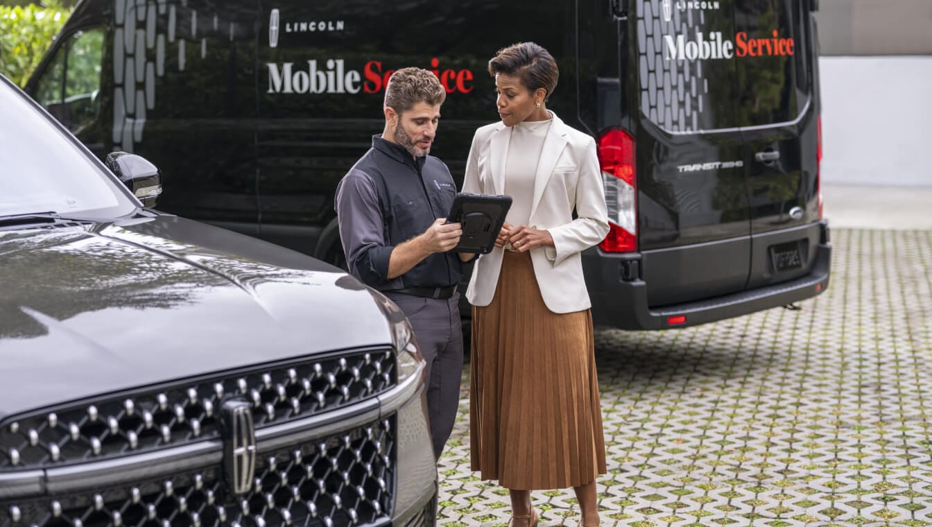 Close-up view of a service technician reviewing tablet data with a client next to a Lincoln Navigator.