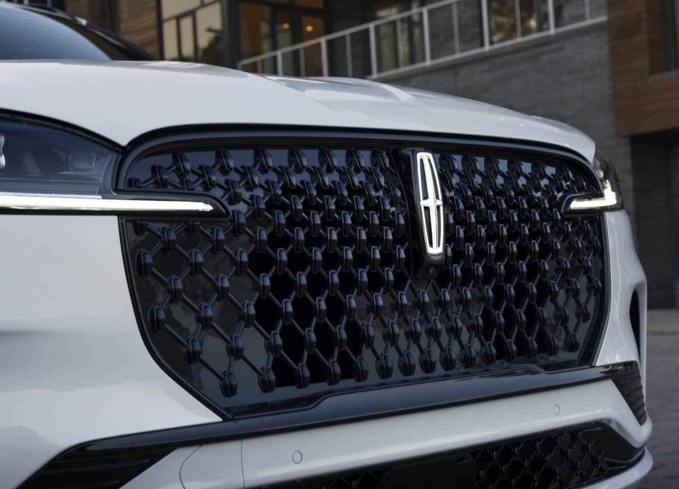Close-up front view of a Lincoln Aviator Reserve mesh grille and illuminated star logo in front of a modern building.