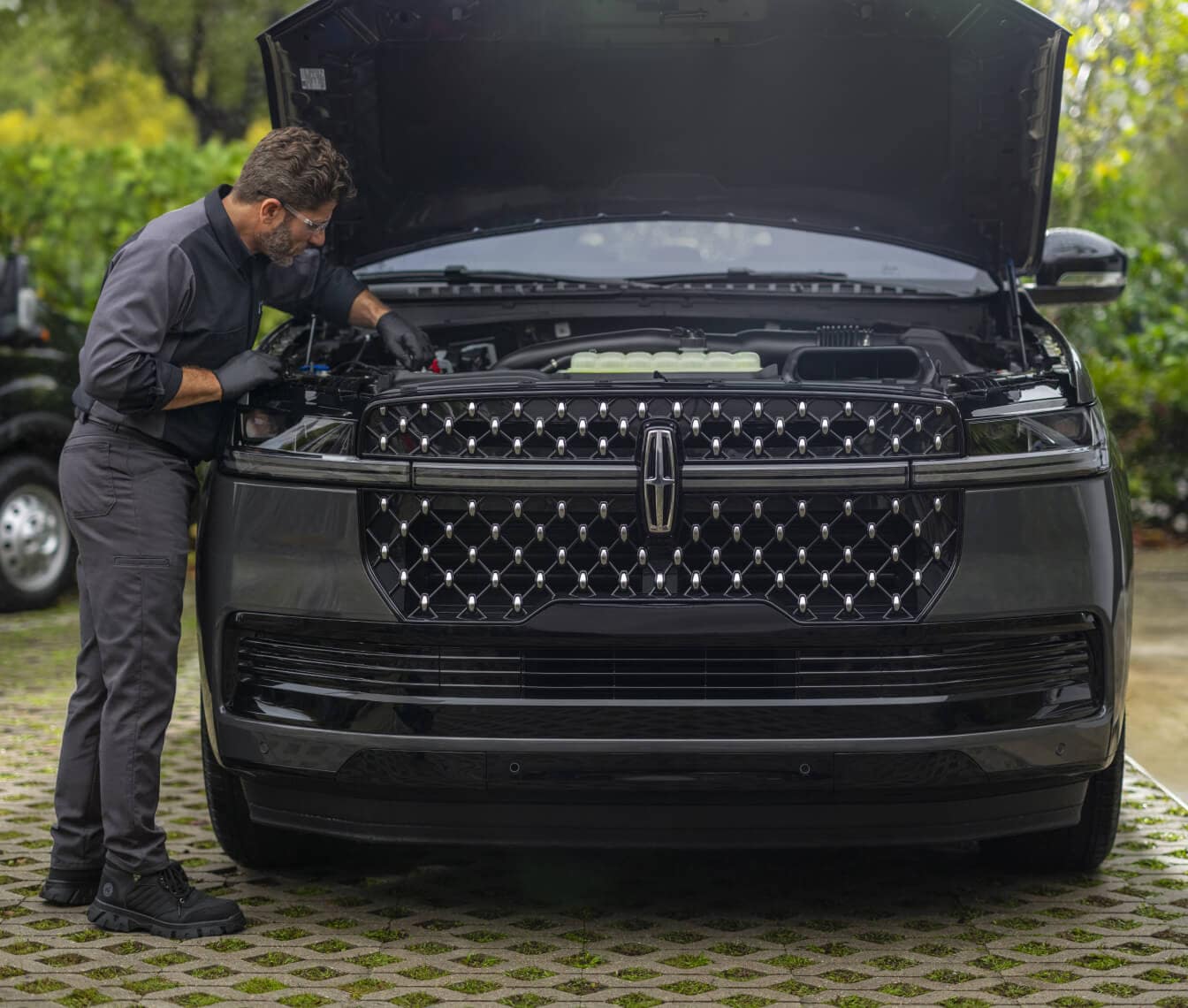Front view of a Lincoln Navigator with its hood open as a technician performs vehicle maintenance outdoors.