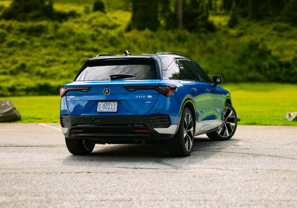 Rear exterior photo of the new Acura ZDX. The SUV is blue and parked in front of grass and trees