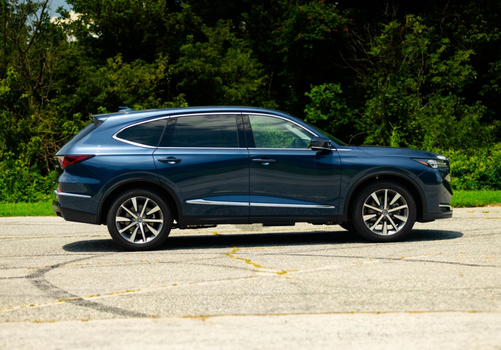 side profile of a 2025 Acura MDX parked in a parking lot with grass and trees behind it
