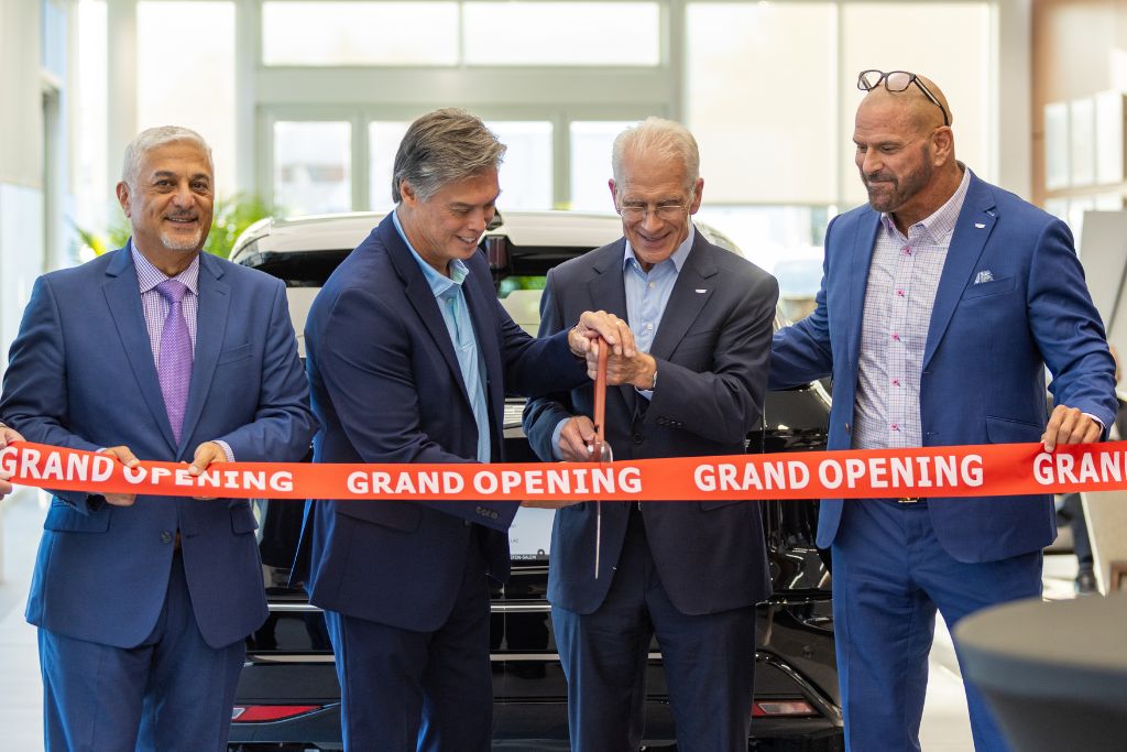 Four men stand behind red ribbon with pair of ceremonial scissors for a grand opening photo at Flow Cadillac of Winston-Salem