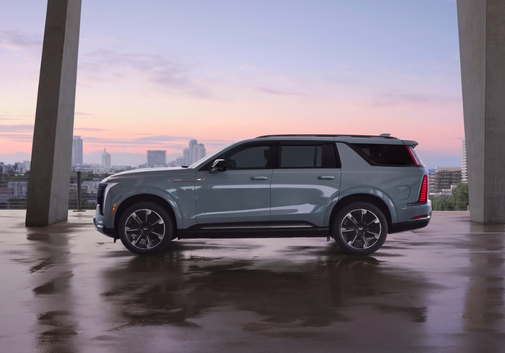 Driver's side of 2025 Cadillac Escalade parked on a paved surface with a sunset in the background