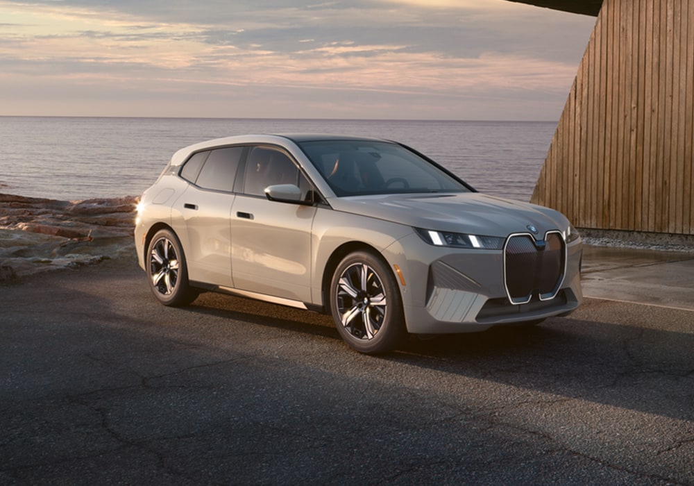 2025 BMW iX parked on a pave surface with a large body of water in the background