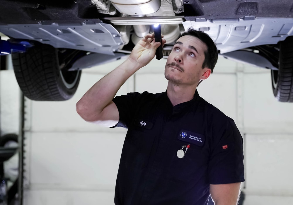 Flow BMW service tech shining a light underneath a lifted car