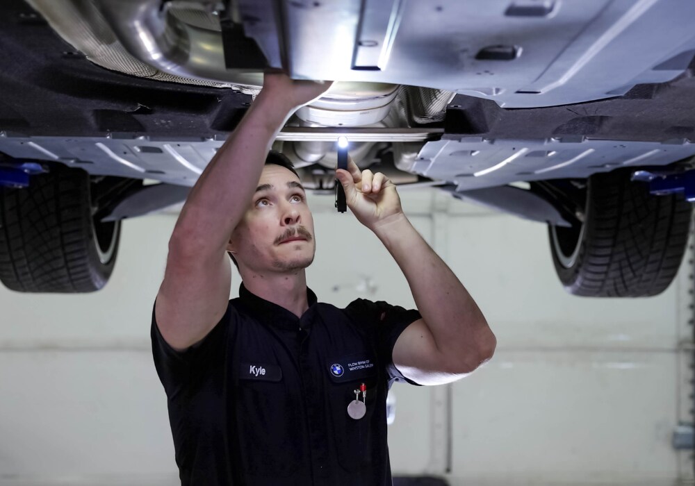 Flow BMW service employee looking underneath the body of a car with a flashlight