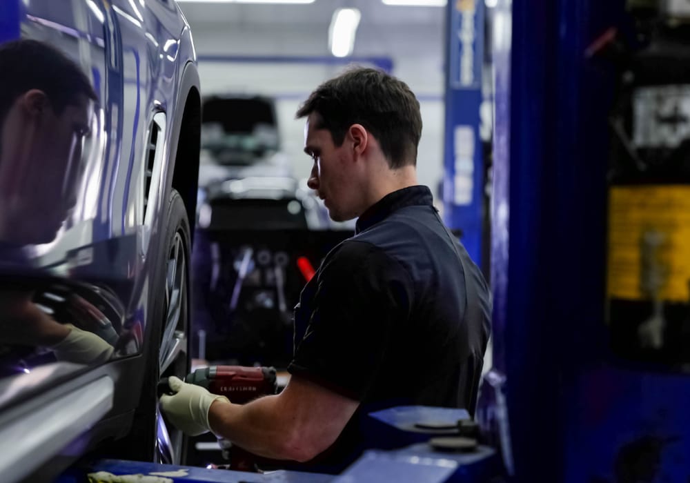 BMW service technician working on the front tire of a car in the service bay