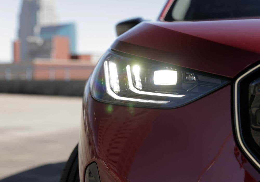 Clsoe up of one headlight of the BMW X3 turned on. The car is red