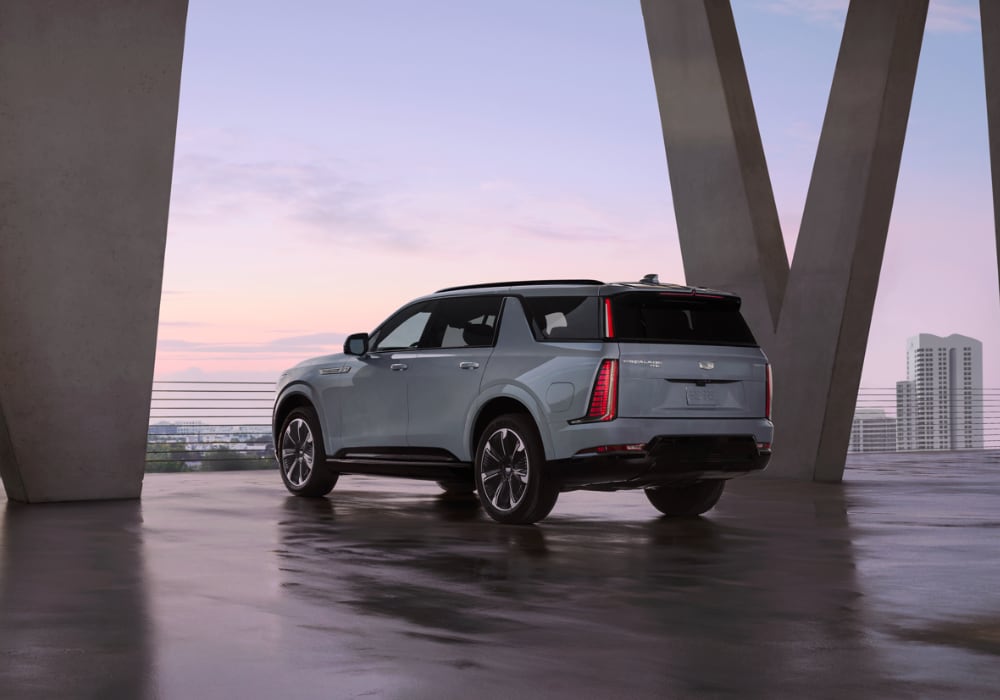Rear 3/4 view of the 2025 Cadillac Escalade SUV parked with tall buildings in the background