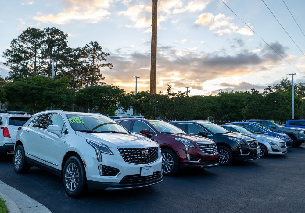 Lineup of Cadillac cars in a parking lot with a sunset in the background