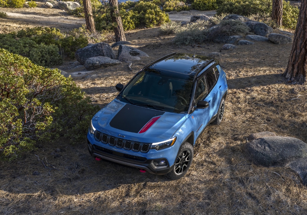 2025 Jeep Compass driving through a wooded area with its headlights on