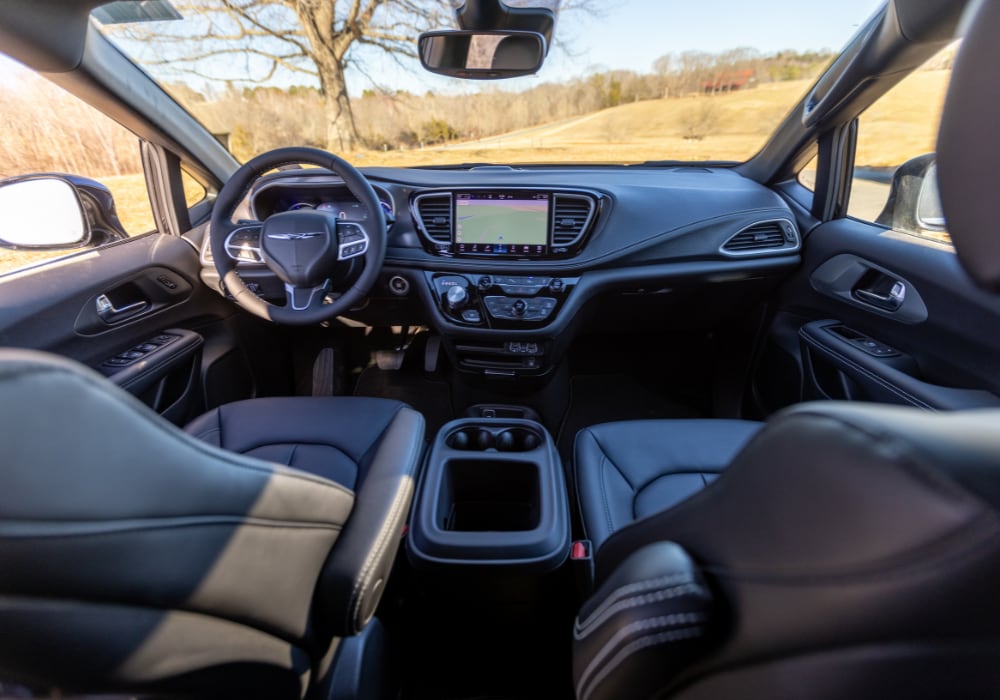 The interior of a new Chrysler Pacifica showing the infotainment center and front dash of the car. The photo was taken from the back seat showing the front seats