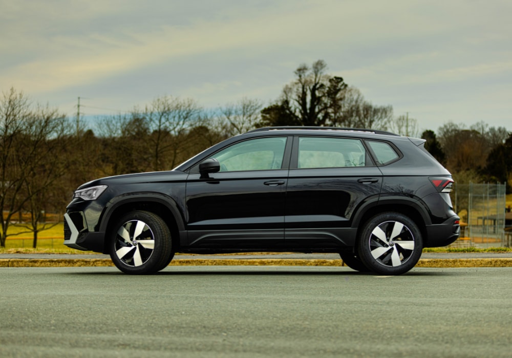 New Volkswagen Taos driver's side view. The car is parked on a paved surface with trees in the background