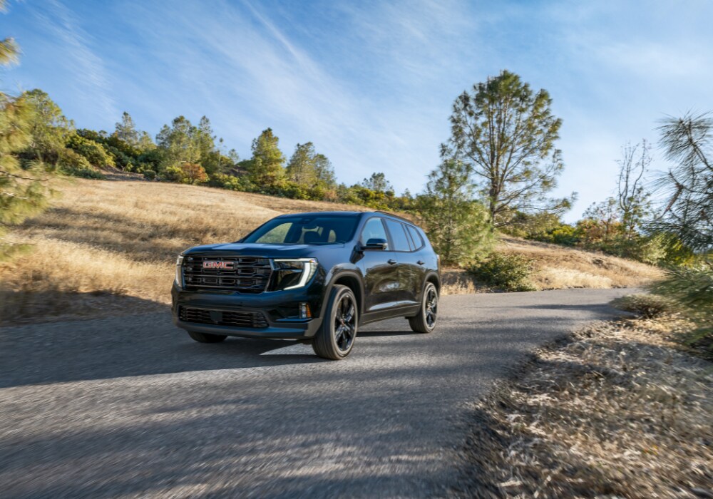 Black 2026 GMC Terrain SUV driving down a road with trees in the background