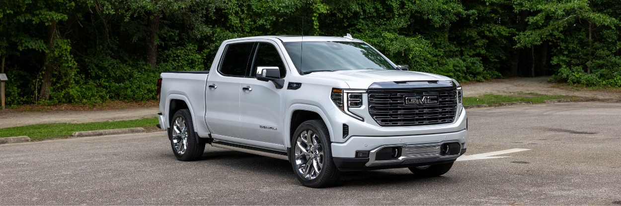 White 2024 GMC Sierra 1500 parked on a paveed lot in front of trees