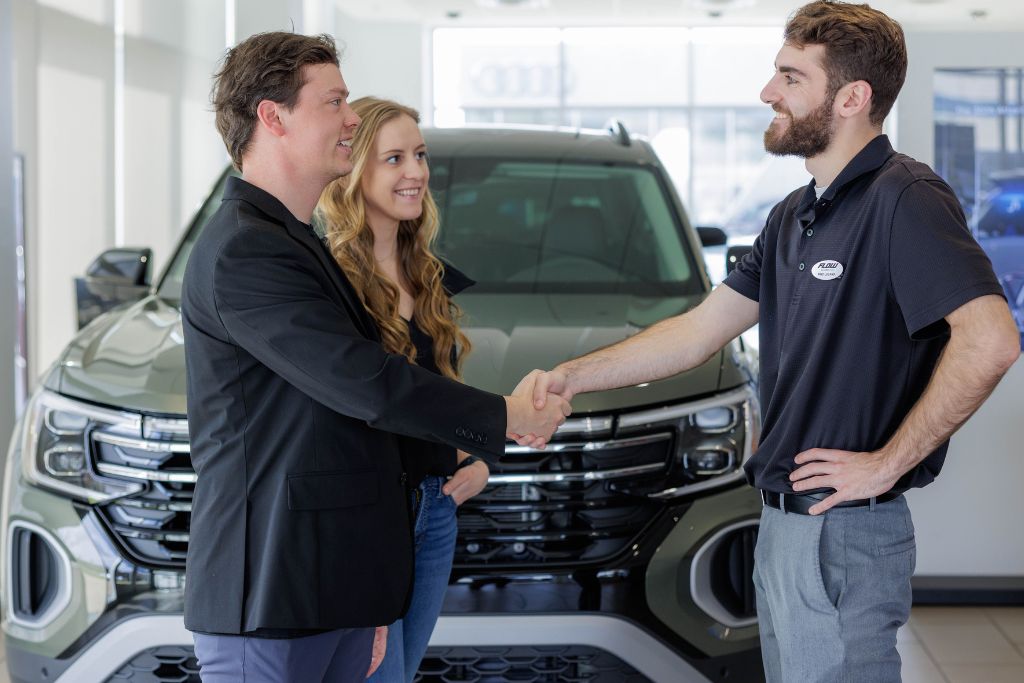 Man and woman shaking hands with sales person at car dealership