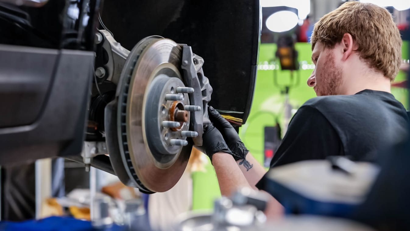 Image shows Flow GMC Buick Greensboro service center employee inspecting the brake pads of a car in the service center