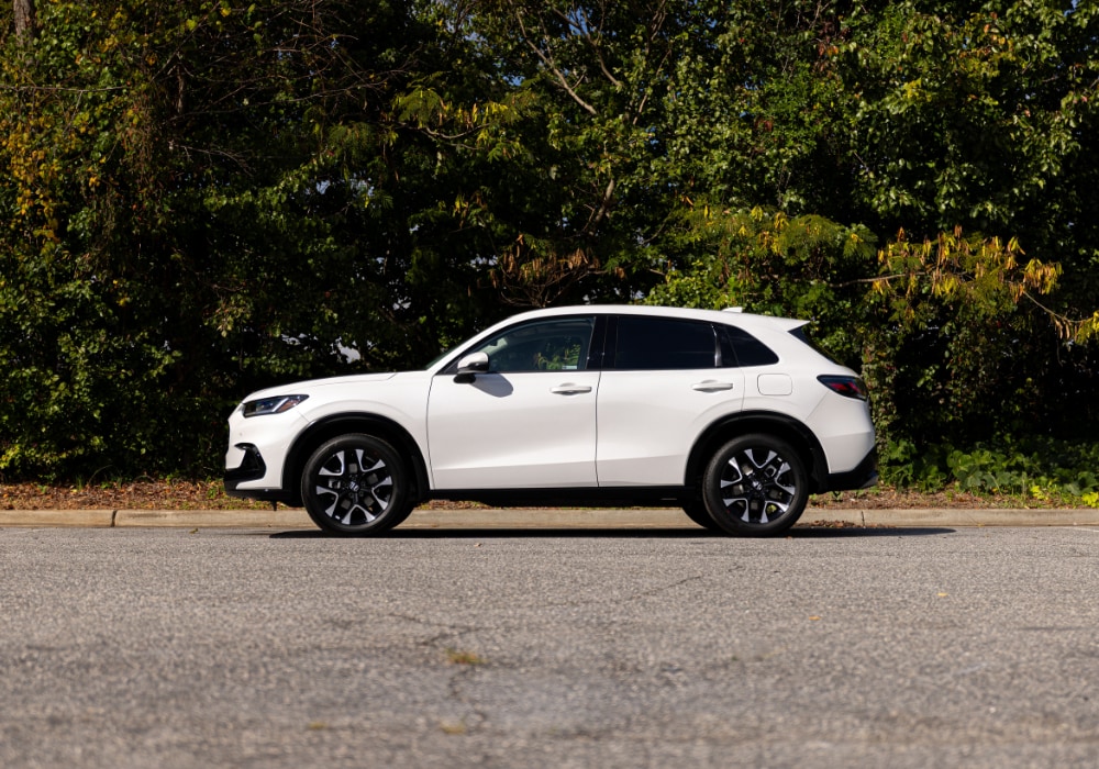Passenger side view of a 2025 Honda CR-V parked on a paved surface with trees in the background