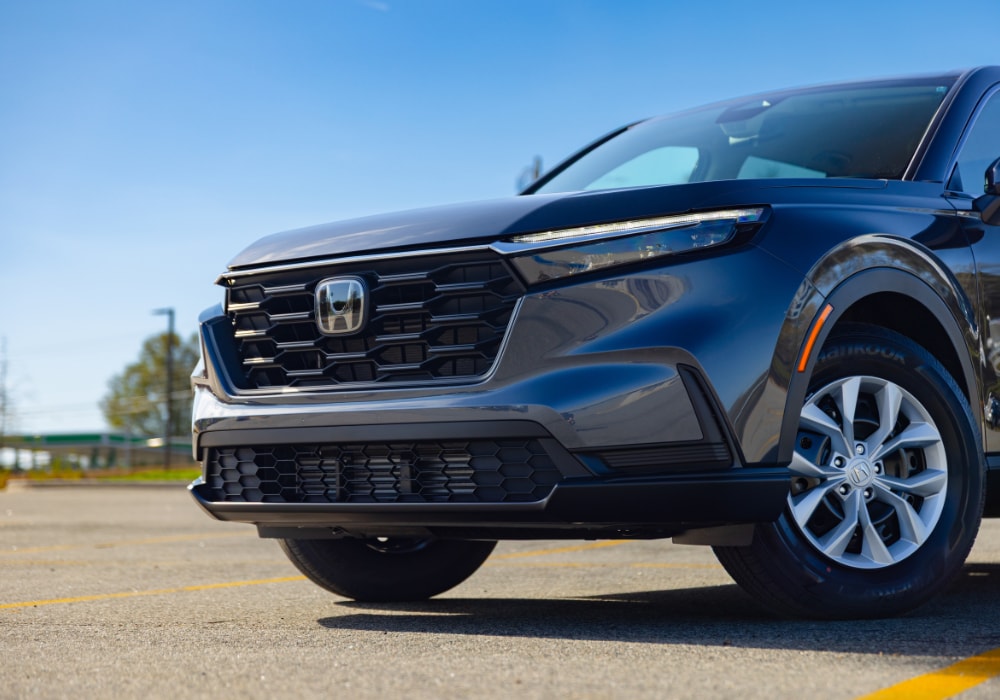 Close up photo of the front grille of a 2026 Honda CR-V. The SUV is gray with a blue sky in the background
