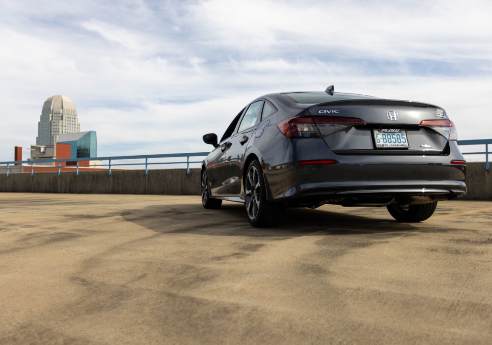 2025-hybrid-honda-civic.png Photo shows the 2025 Honda Civic Hybrid from the rear exterior angle. The honda logo is visible on the trunk and there is a cloudy sky in the background